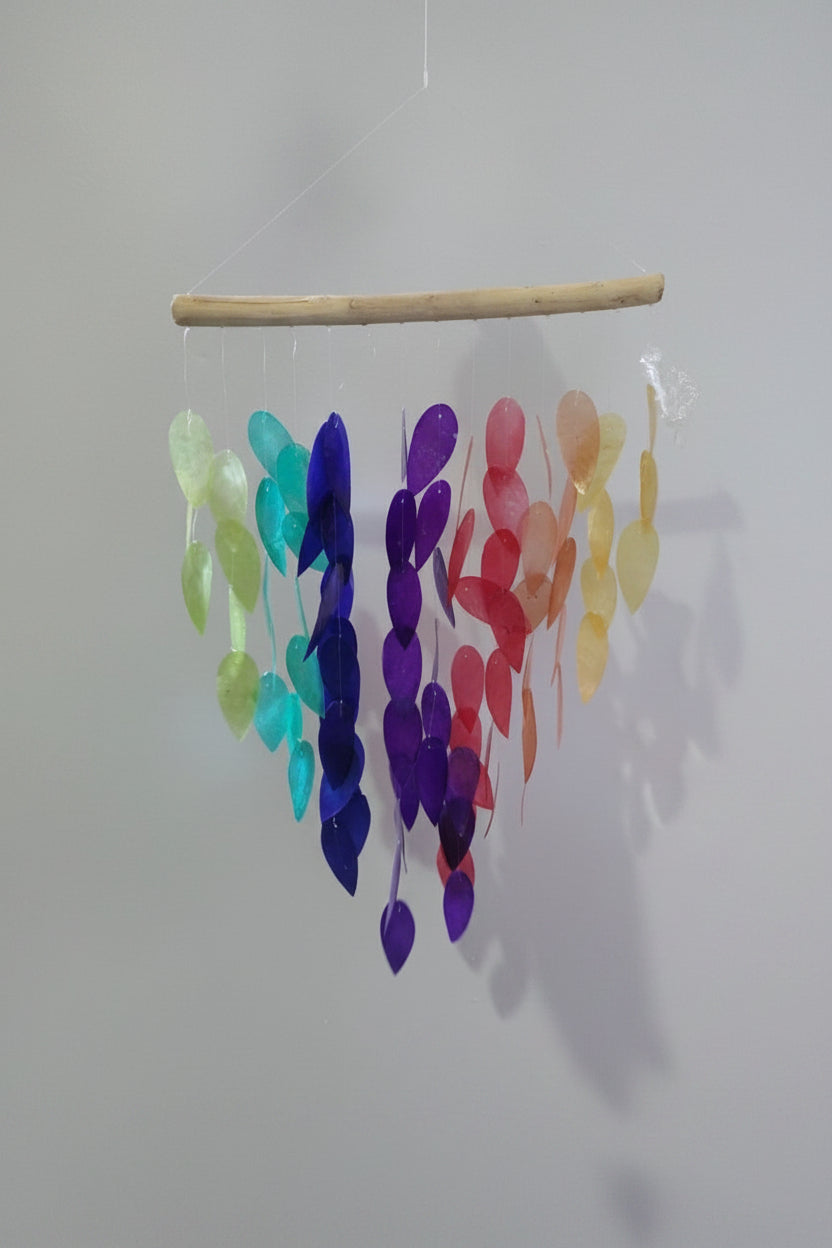 Colorful glass leaf mobile hanging from a branch against a white background