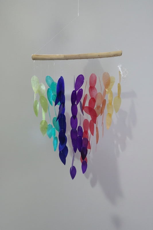Colorful glass leaf mobile hanging from a branch against a white background